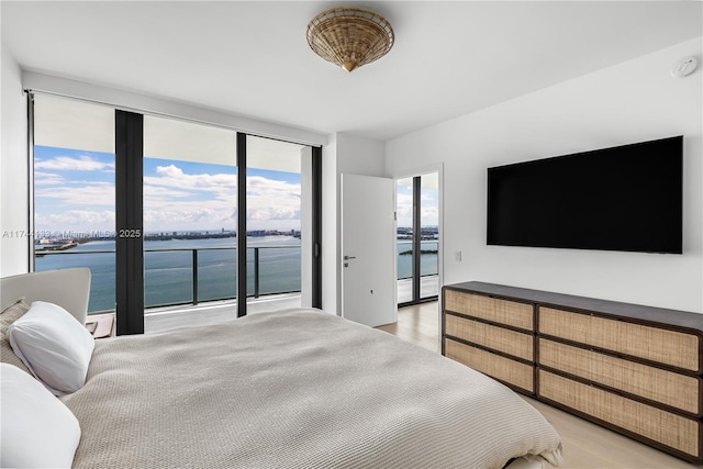 bedroom with access to exterior, light wood-type flooring, a water view, and expansive windows