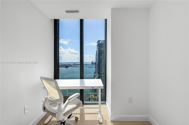 office with a wall of windows, visible vents, baseboards, and wood finished floors