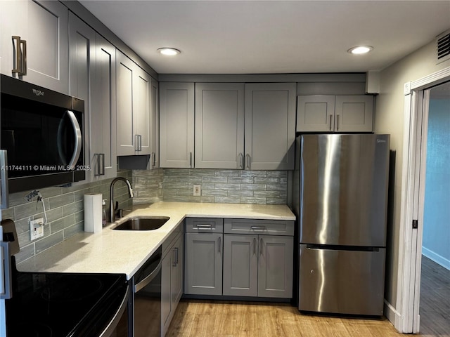 kitchen featuring sink, appliances with stainless steel finishes, gray cabinetry, tasteful backsplash, and light hardwood / wood-style floors