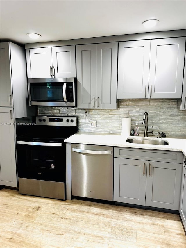 kitchen featuring sink, gray cabinetry, tasteful backsplash, light hardwood / wood-style flooring, and appliances with stainless steel finishes