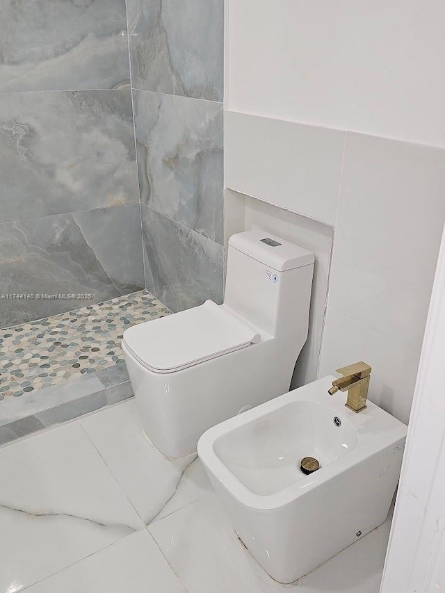 bathroom with toilet, sink, tile walls, a tile shower, and a bidet