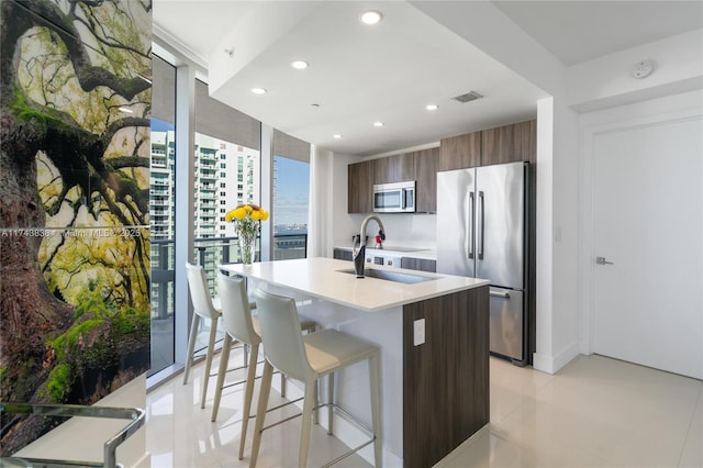 kitchen featuring sink, expansive windows, an island with sink, and appliances with stainless steel finishes