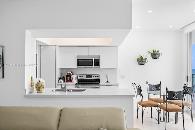 kitchen with appliances with stainless steel finishes, kitchen peninsula, sink, and white cabinets