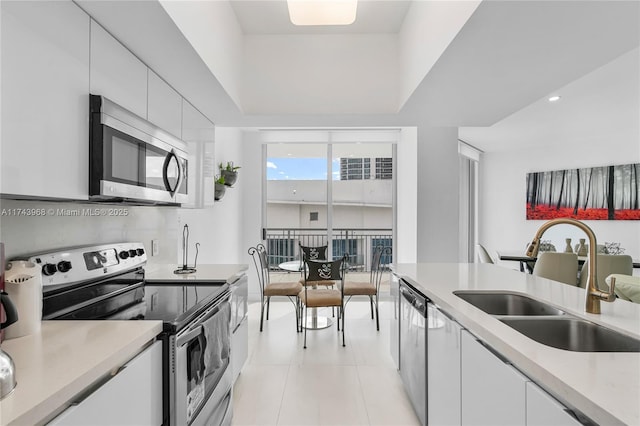 kitchen with sink, light tile patterned floors, appliances with stainless steel finishes, expansive windows, and white cabinets