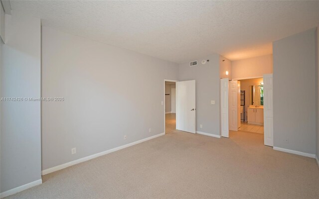 3300 NE 192nd St Unit 111, Aventura, FL 33180 - unfurnished bedroom featuring light colored carpet, a textured ceiling, baseboards, and connected bathroom