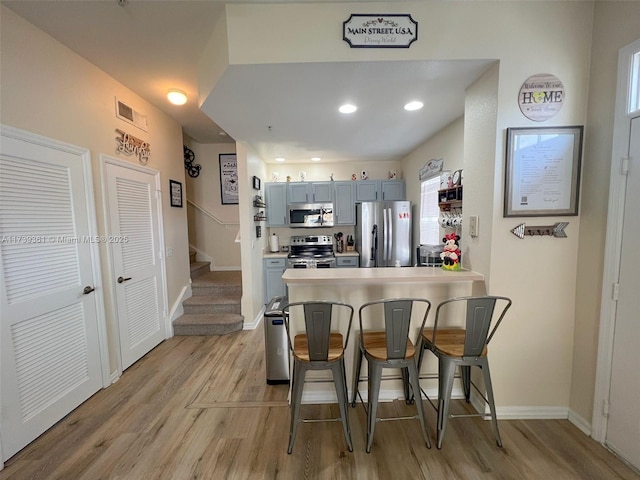 kitchen featuring gray cabinetry, a kitchen bar, light hardwood / wood-style floors, and appliances with stainless steel finishes