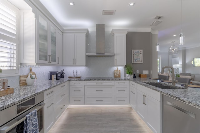 kitchen featuring wall chimney exhaust hood, sink, light stone counters, decorative light fixtures, and white cabinets