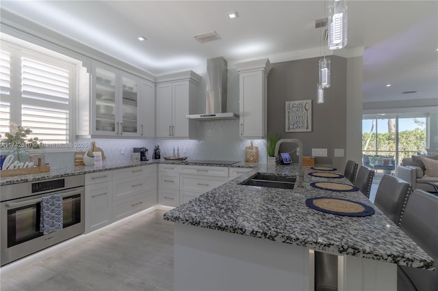 kitchen with pendant lighting, sink, white cabinetry, oven, and wall chimney exhaust hood