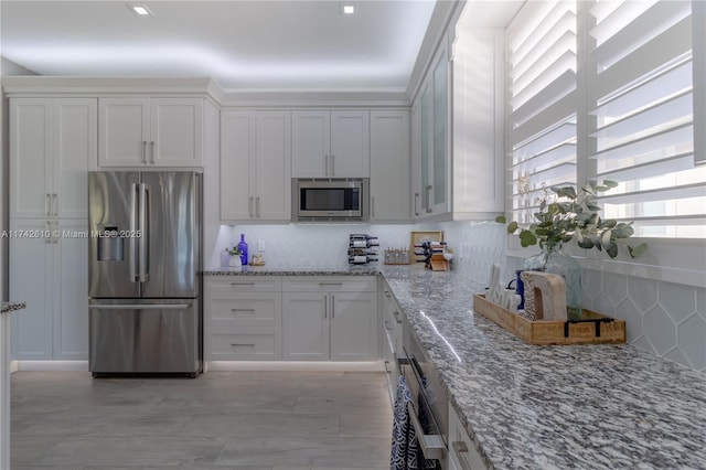 kitchen with appliances with stainless steel finishes, light stone countertops, decorative backsplash, and white cabinets