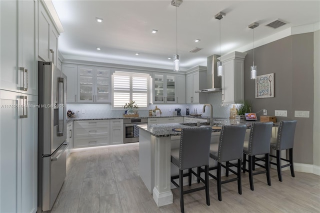 kitchen with pendant lighting, a breakfast bar area, appliances with stainless steel finishes, dark stone countertops, and wall chimney exhaust hood