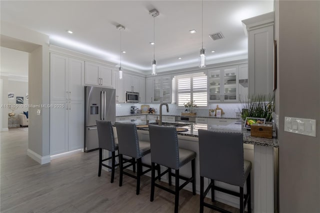 kitchen with white cabinetry, a kitchen breakfast bar, dark stone counters, stainless steel appliances, and light hardwood / wood-style flooring