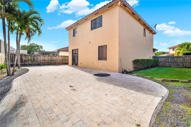 back of house featuring a fenced backyard, a tile roof, a lawn, stucco siding, and a patio area