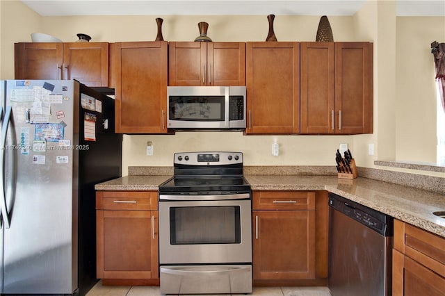kitchen featuring brown cabinets, light tile patterned floors, light stone countertops, and stainless steel appliances