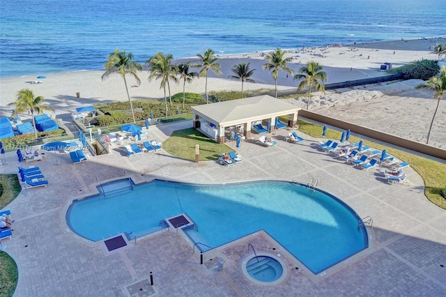 view of swimming pool with a water view, a view of the beach, and a patio