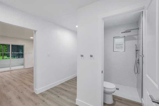 bathroom with hardwood / wood-style flooring, tiled shower, and toilet