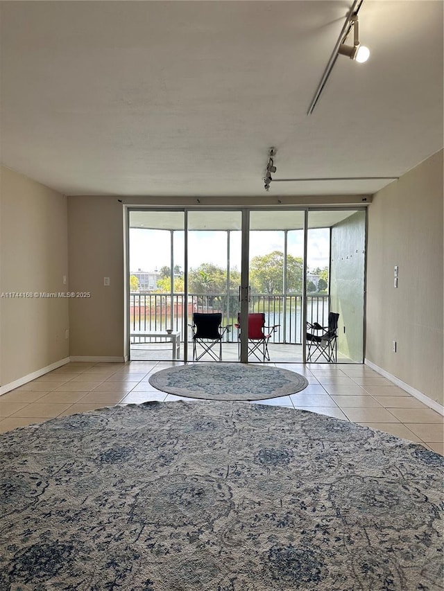 unfurnished living room featuring floor to ceiling windows, a water view, track lighting, and light tile patterned floors