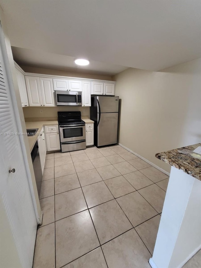 kitchen with light tile patterned floors, sink, stainless steel appliances, light stone counters, and white cabinets