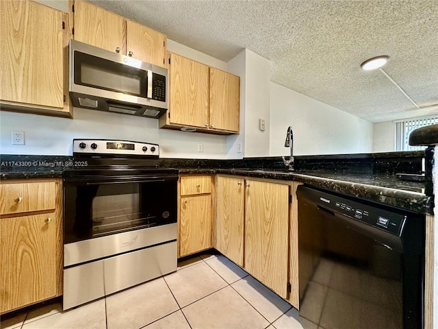 kitchen with light tile patterned floors, appliances with stainless steel finishes, a textured ceiling, dark stone counters, and light brown cabinets