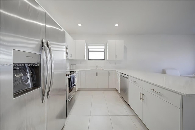 kitchen with light countertops, appliances with stainless steel finishes, a peninsula, light tile patterned flooring, and a sink