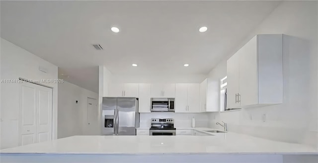 kitchen featuring a peninsula, stainless steel appliances, light countertops, and a sink