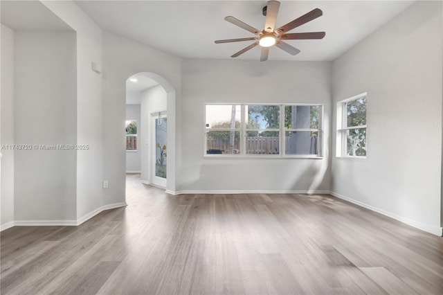 empty room with a ceiling fan, baseboards, arched walkways, and wood finished floors