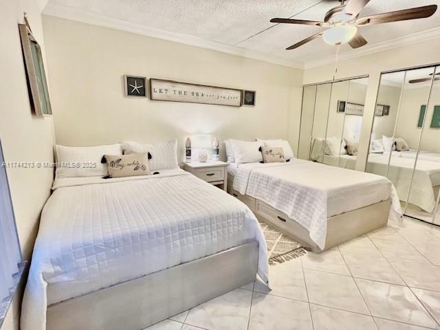 bedroom with light tile patterned floors, ceiling fan, ornamental molding, a textured ceiling, and two closets