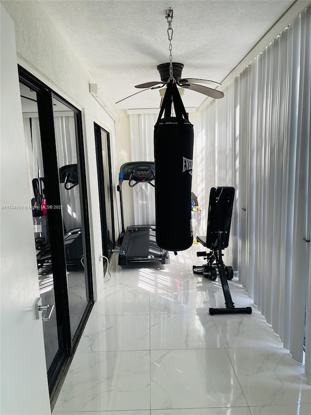 exercise room with ceiling fan and a textured ceiling