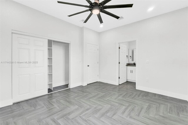 unfurnished bedroom featuring light parquet flooring, ensuite bathroom, ceiling fan, and a closet