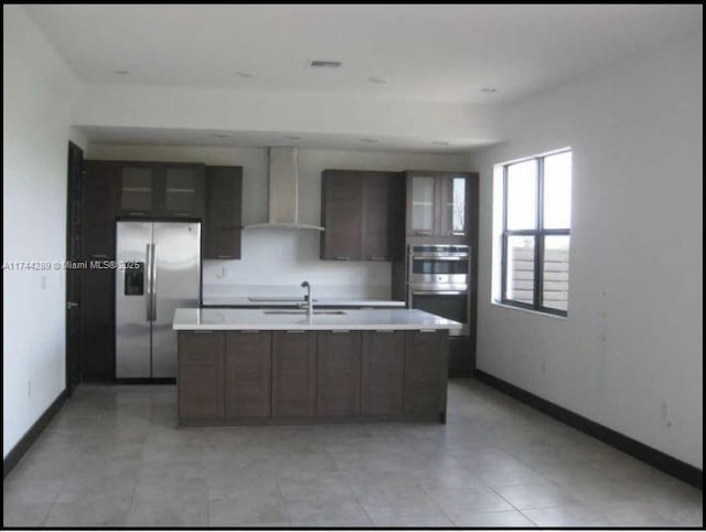 kitchen featuring wall chimney range hood, appliances with stainless steel finishes, light countertops, and a sink