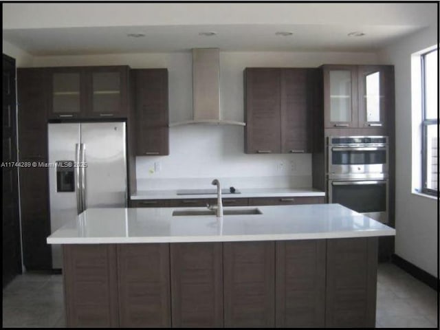 kitchen with wall chimney range hood, appliances with stainless steel finishes, a sink, and light countertops