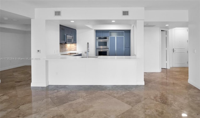 kitchen with appliances with stainless steel finishes, blue cabinets, sink, backsplash, and kitchen peninsula