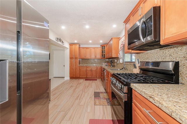 kitchen featuring stainless steel appliances, a sink, light stone countertops, tasteful backsplash, and glass insert cabinets