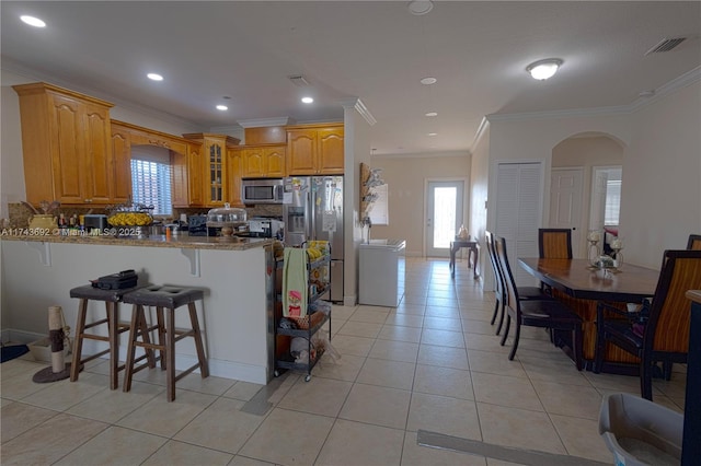 kitchen with light tile patterned floors, crown molding, a breakfast bar, appliances with stainless steel finishes, and kitchen peninsula