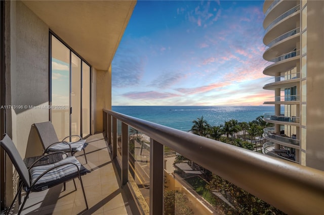 balcony at dusk featuring a water view