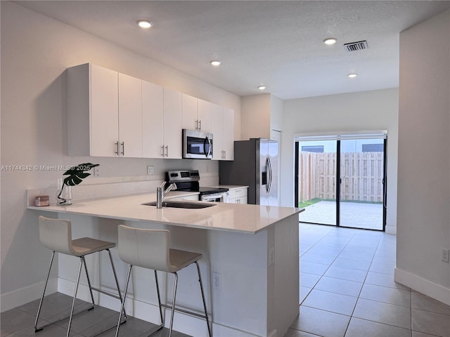 kitchen with a breakfast bar area, light tile patterned floors, appliances with stainless steel finishes, kitchen peninsula, and white cabinets