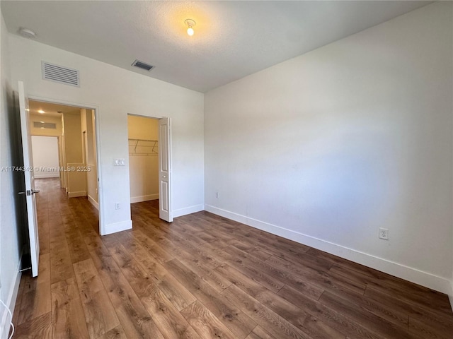 unfurnished bedroom featuring a spacious closet, hardwood / wood-style floors, a textured ceiling, and a closet