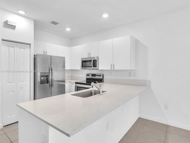 kitchen with sink, light tile patterned floors, appliances with stainless steel finishes, kitchen peninsula, and white cabinets