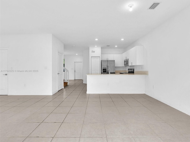 kitchen with stainless steel appliances, kitchen peninsula, light tile patterned floors, and white cabinets