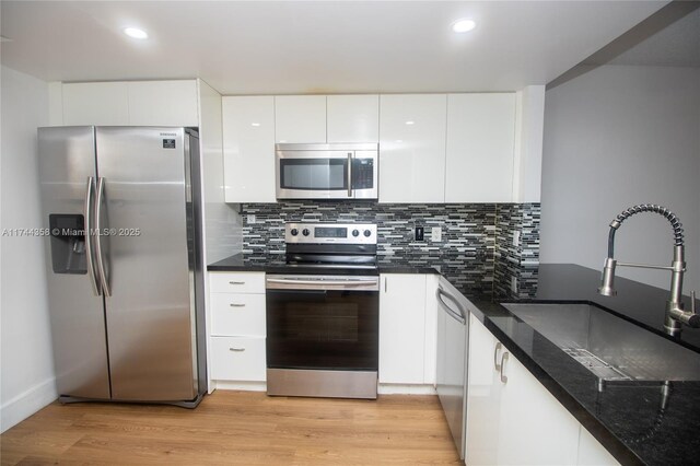 kitchen featuring light wood-style flooring, tasteful backsplash, white cabinets, a sink, and stainless steel appliances
