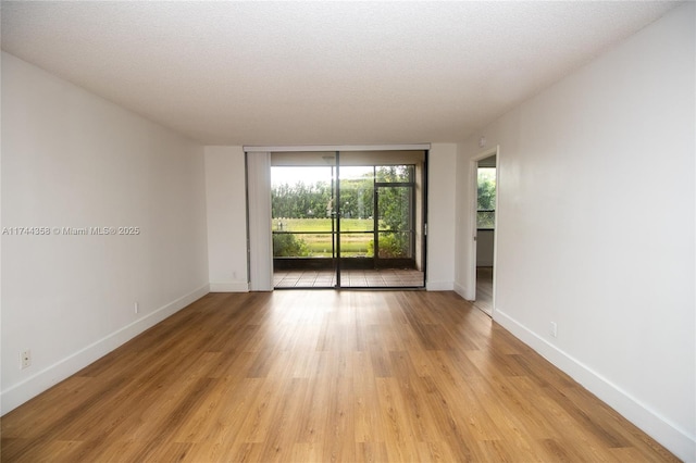 empty room featuring floor to ceiling windows, light wood-style flooring, baseboards, and a textured ceiling