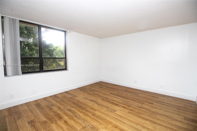 empty room with a textured ceiling, baseboards, and wood finished floors