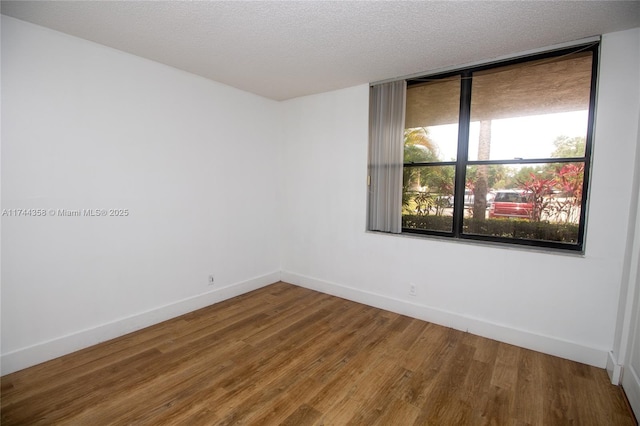 unfurnished room with baseboards, a textured ceiling, and wood finished floors