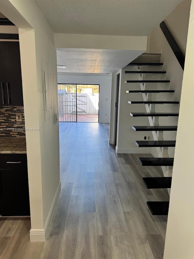 corridor with stairs, a textured ceiling, baseboards, and wood finished floors