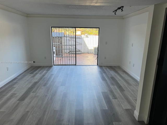 empty room featuring a textured ceiling, wood finished floors, baseboards, rail lighting, and crown molding