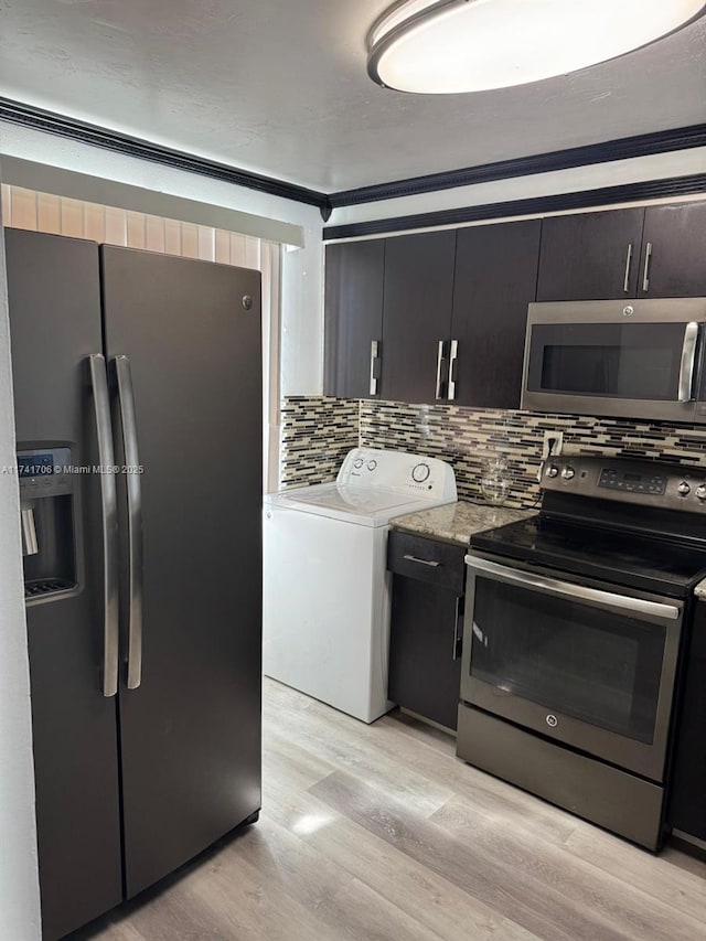 kitchen with appliances with stainless steel finishes, washer / clothes dryer, light hardwood / wood-style flooring, and backsplash