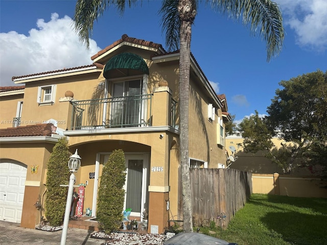 view of front of house featuring a garage, a balcony, a tiled roof, fence, and stucco siding