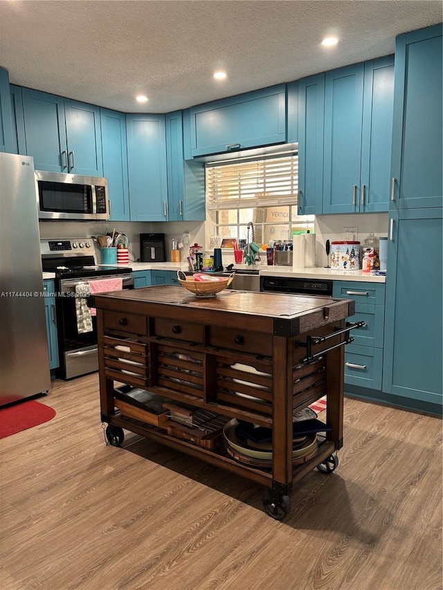 kitchen with light wood-type flooring, blue cabinetry, and appliances with stainless steel finishes