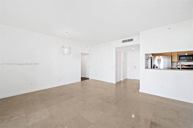 unfurnished living room featuring a notable chandelier, baseboards, visible vents, and a sink