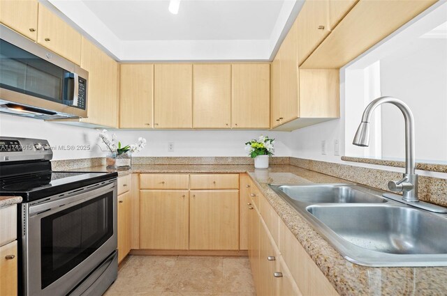 kitchen with light stone countertops, appliances with stainless steel finishes, a sink, and light brown cabinetry