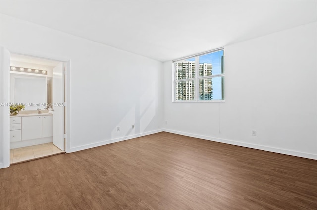 unfurnished bedroom with ensuite bath, baseboards, and wood finished floors